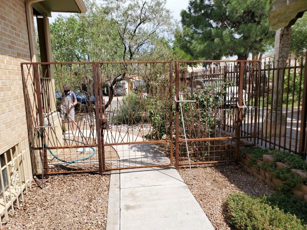 A person installs a decorative metal gate across a sidewalk between a brick house and a garden fence.