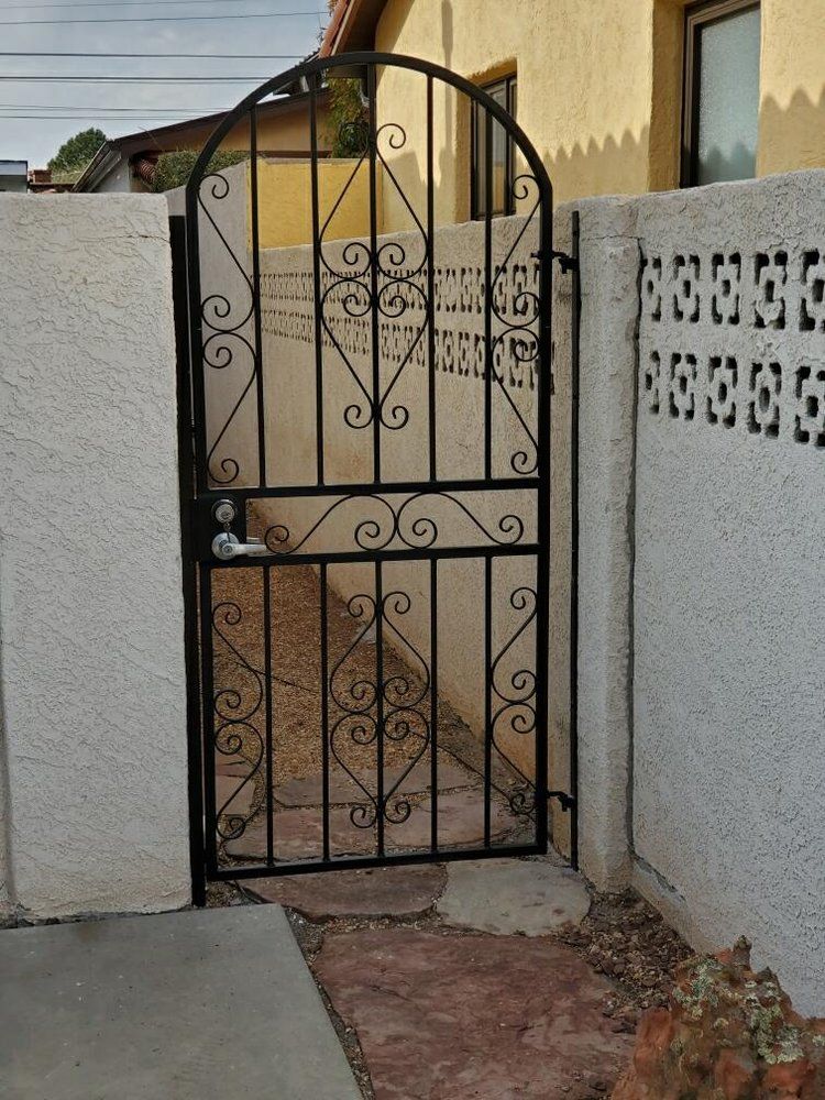 An arched black wrought iron gate set between two white stucco walls on a stone path.
