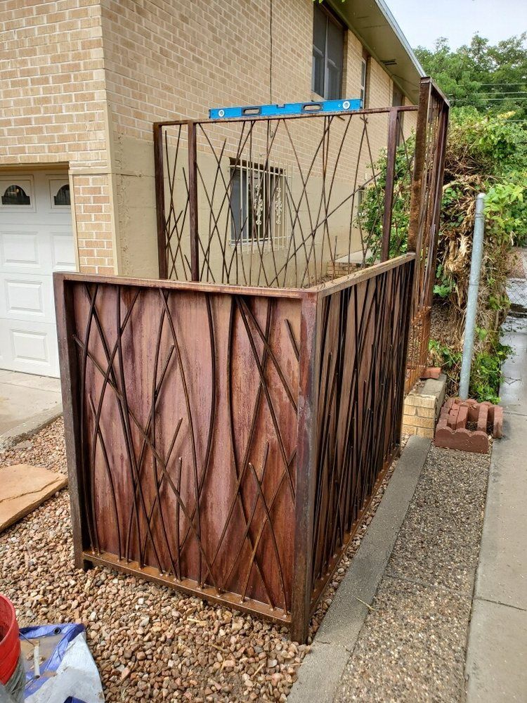 A rectangular outdoor privacy screen featuring a wood frame and a decorative, twig-like lattice design on a gravel ground.