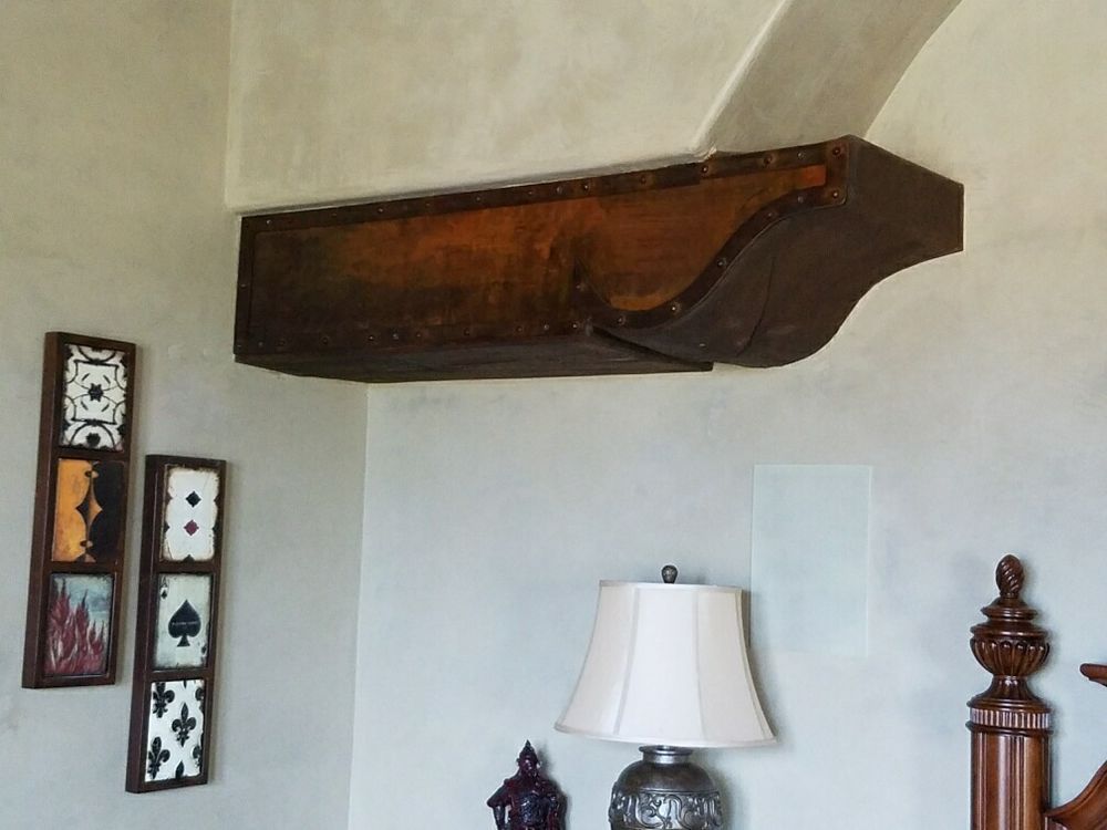 A dark wood corbel attached to a light-colored wall above a bedroom lamp, next to two vertical wall art panels.