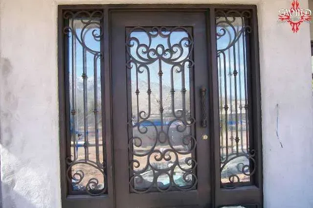 Dark metal decorative front door with glass panels and ornate ironwork on a white wall