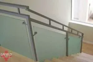 A staircase featuring a modern silver metal handrail and frosted glass panels, set in a bright, minimalist interior space.