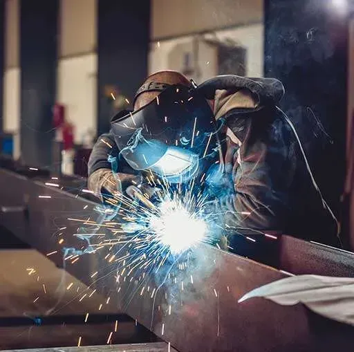 Welder wearing protective mask sparks bright blue light while working on metal in a workshop