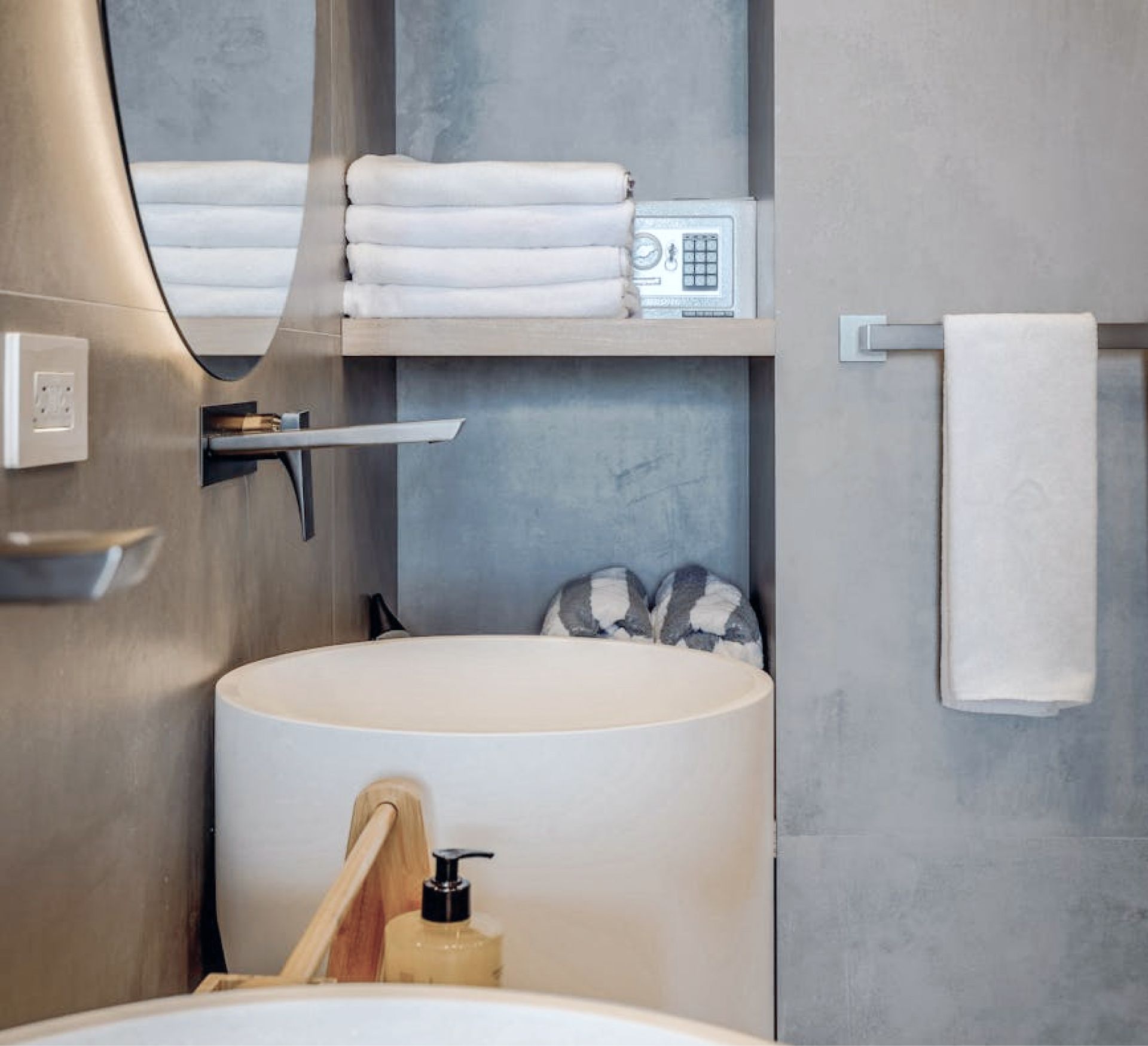 Modern bathroom interior featuring neatly stacked white towels on a shelf, a round sink, and a soap dispenser, emphasizing cleanliness and organization for deep cleaning services.