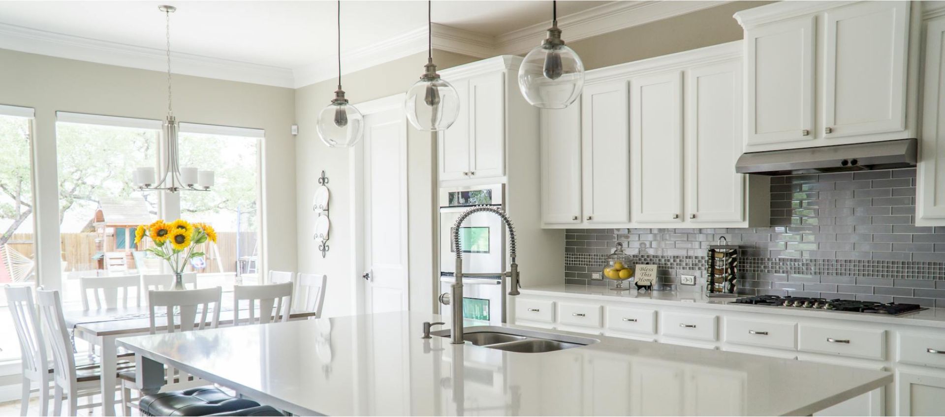 Bright modern kitchen with white cabinetry, stainless steel appliances, and a large island, featuring a vase of sunflowers on the dining table, emphasizing cleanliness and inviting atmosphere for Life Maid Easy's deep cleaning services.