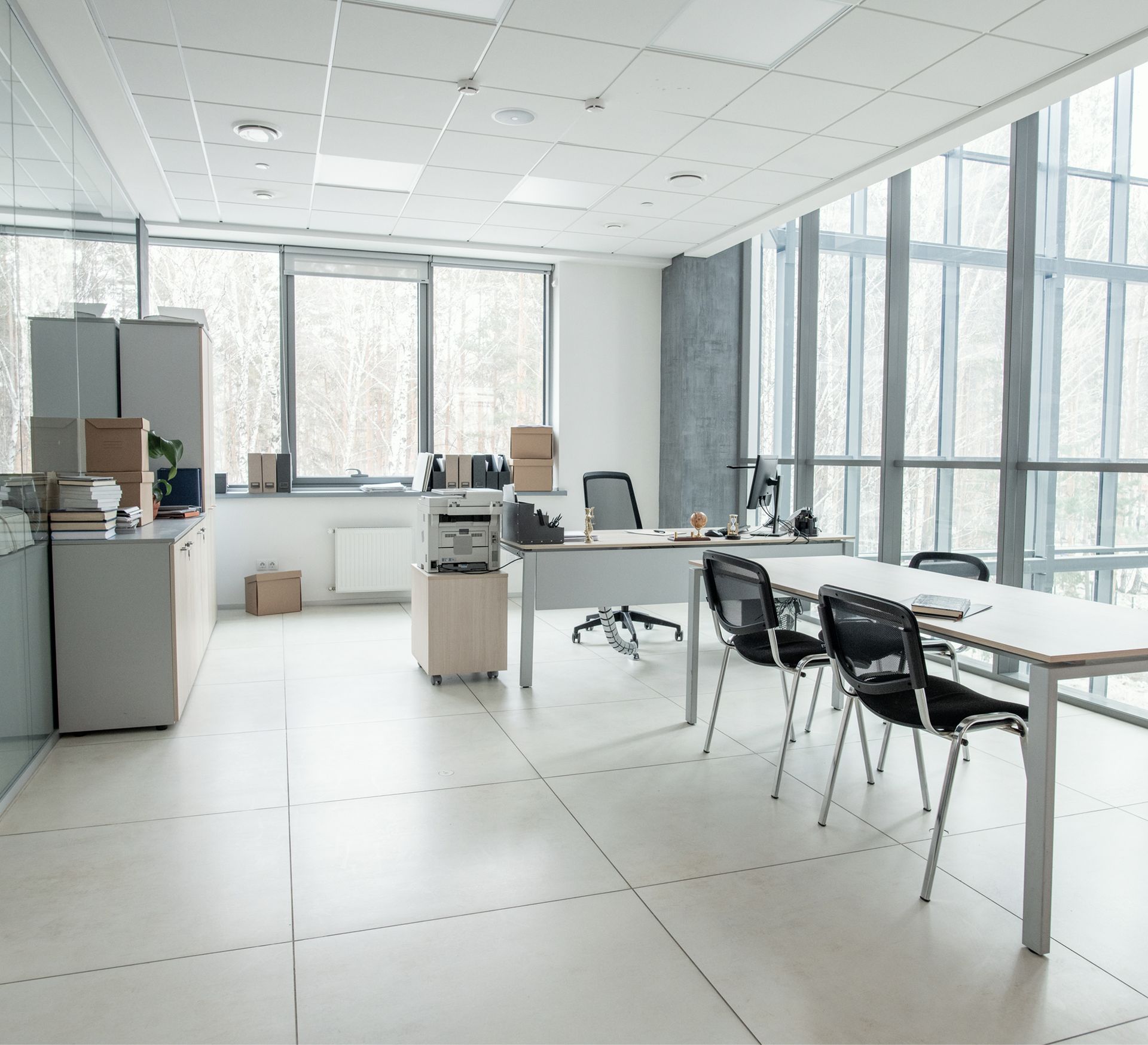 Modern office space with large windows, minimalist furniture, printer, and organized workspace, reflecting professional cleaning services by Life Maid Easy.