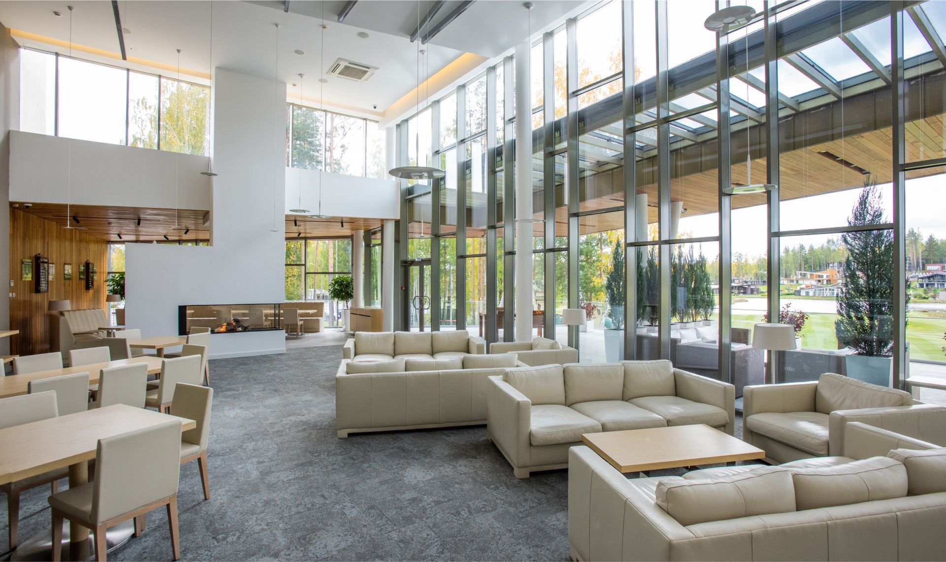 Modern office interior with large windows, comfortable white sofas, wooden tables, and a fireplace, emphasizing a clean and welcoming workspace.