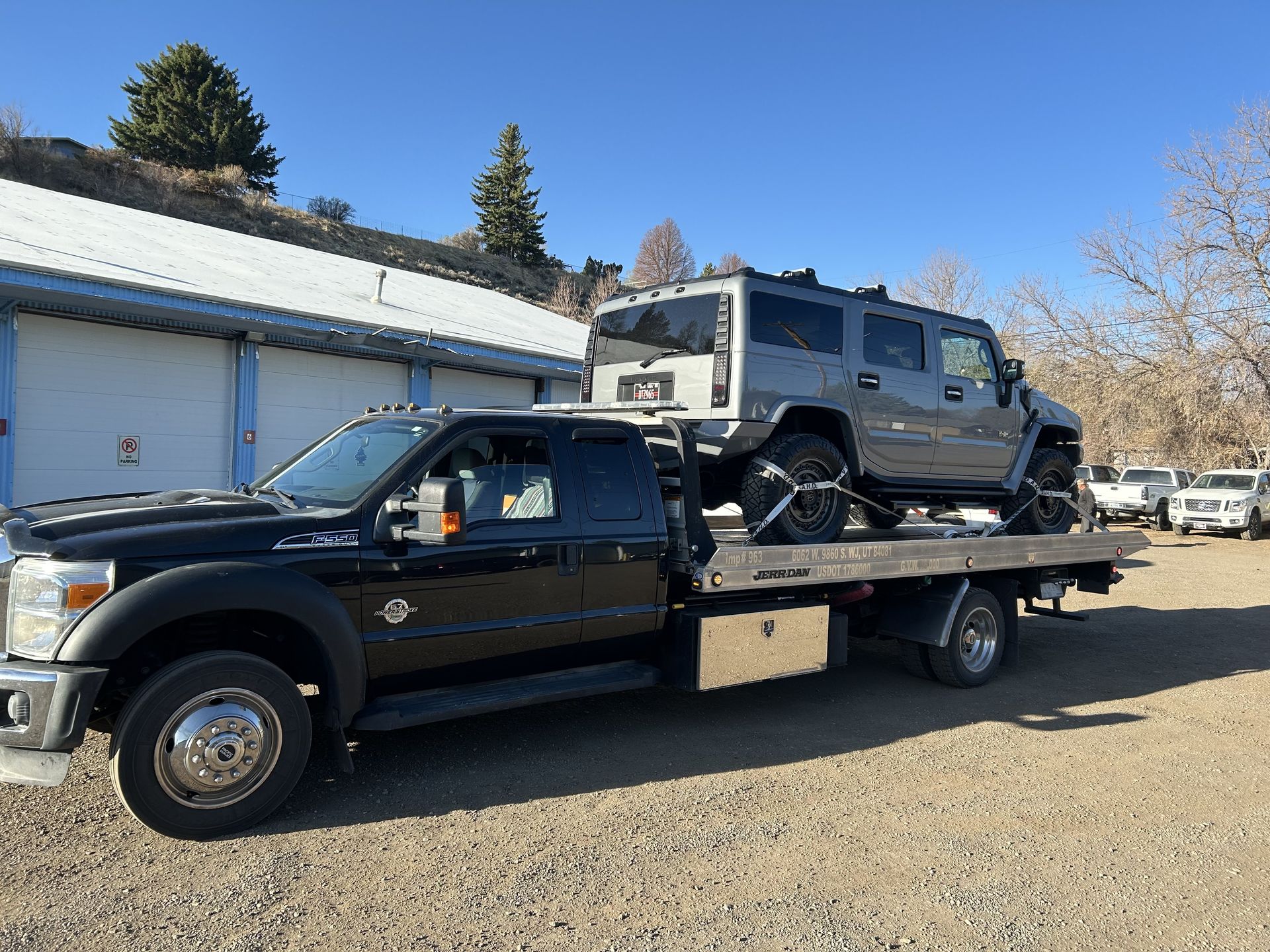 Black tow truck carrying a gray Hummer on a sunny day.