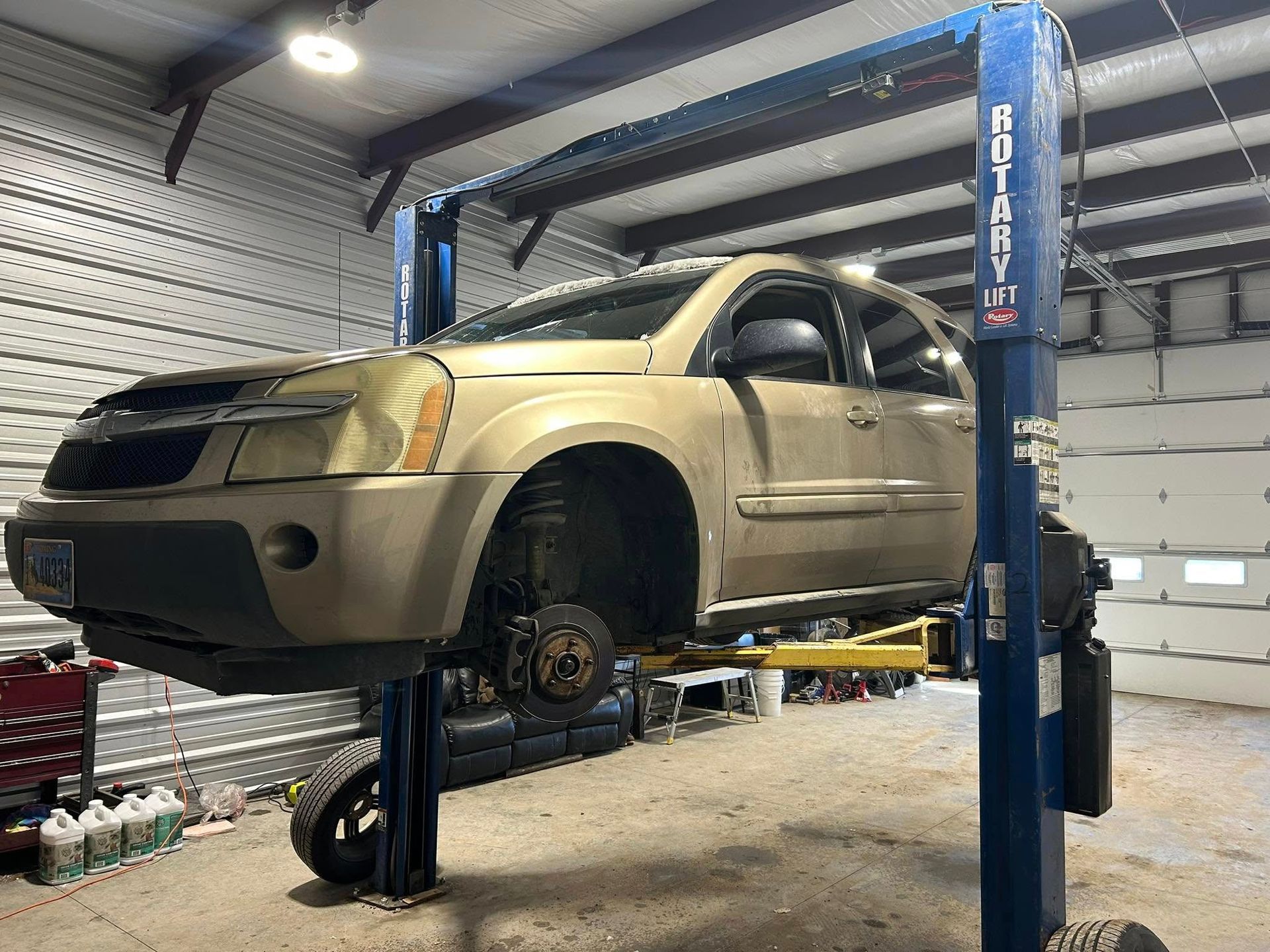A gold SUV is raised on a Rotary lift in a garage. The front left wheel is removed.