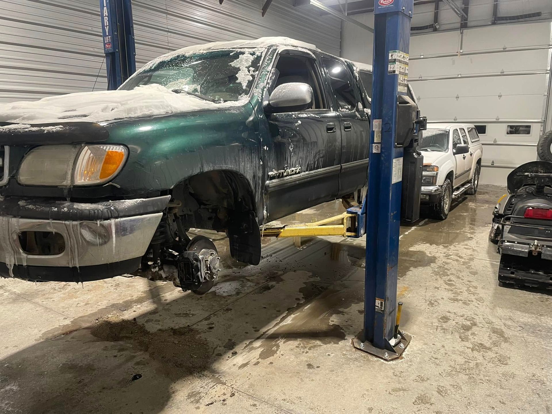 A green SUV on a lift in a garage, with one wheel removed. Snowy conditions are visible.