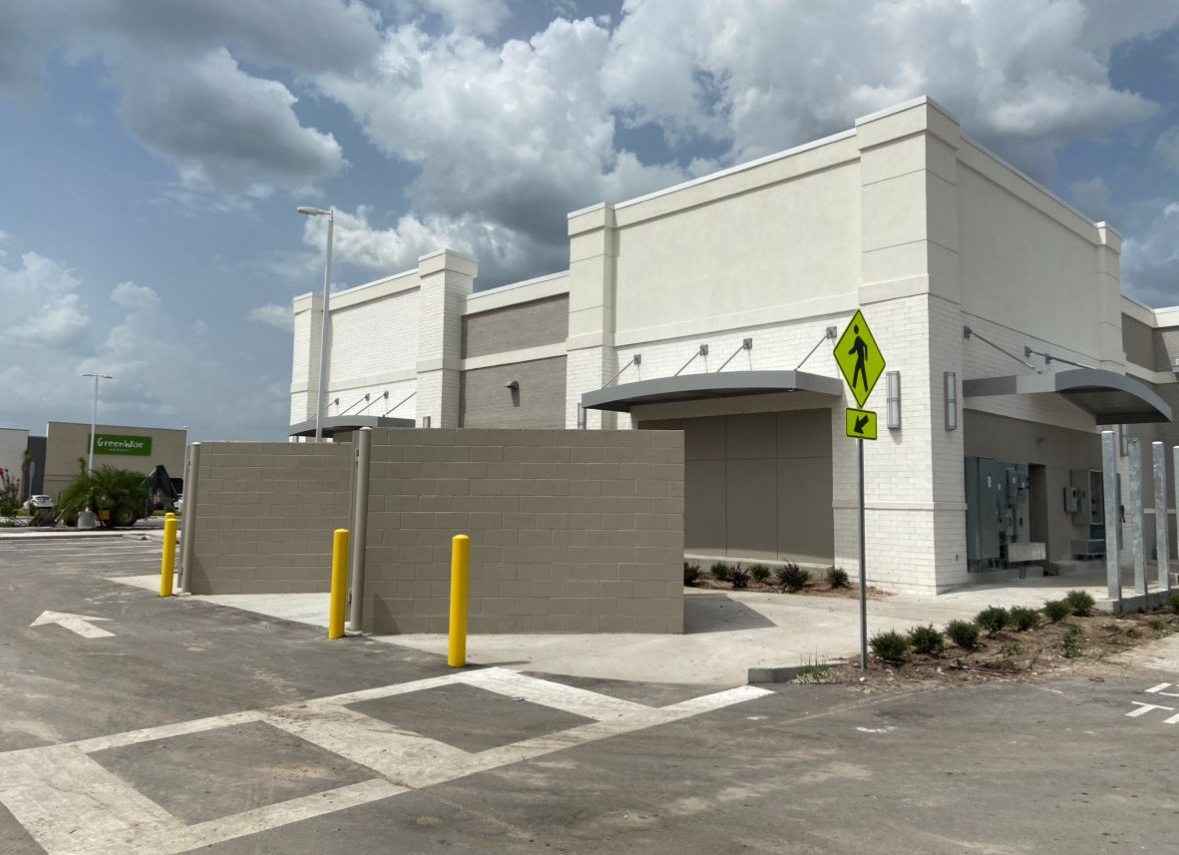 Exterior of a beige and white building with a parking lot and a cloudy sky.