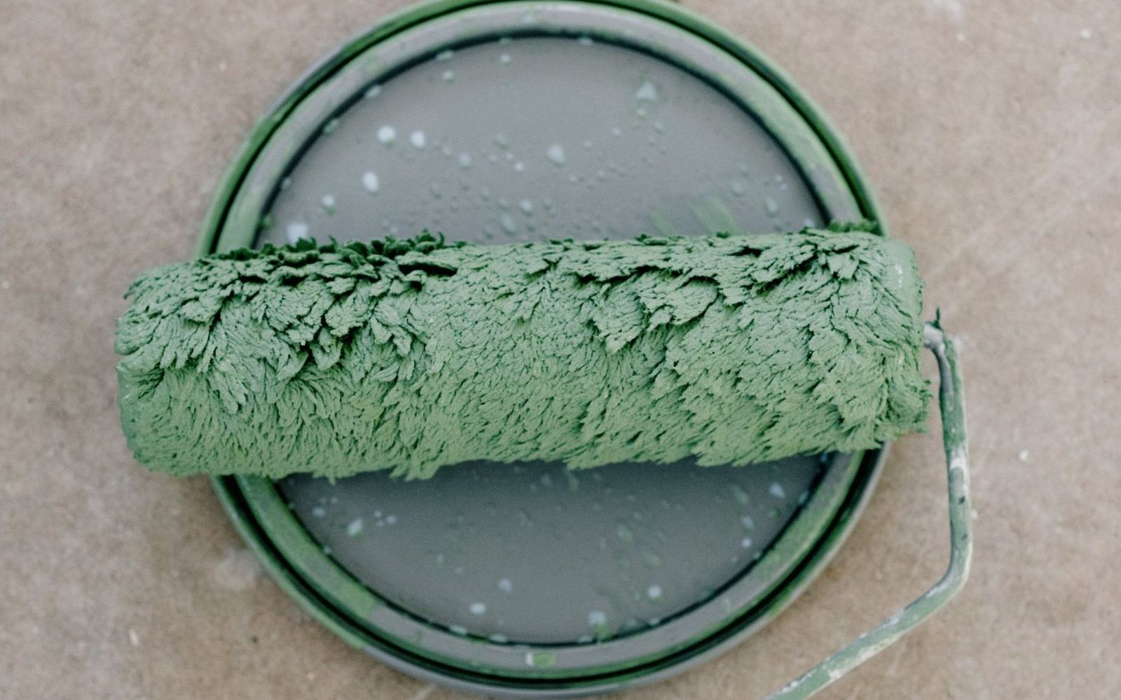 A green paint roller is sitting on top of a green paint can.