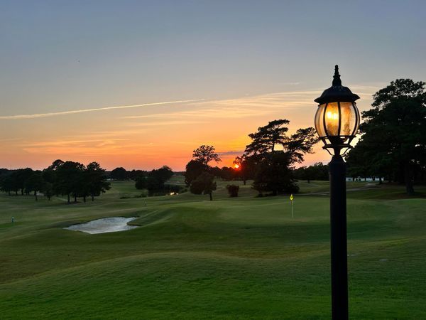 A sunset over a golf course with a lamp post in the foreground