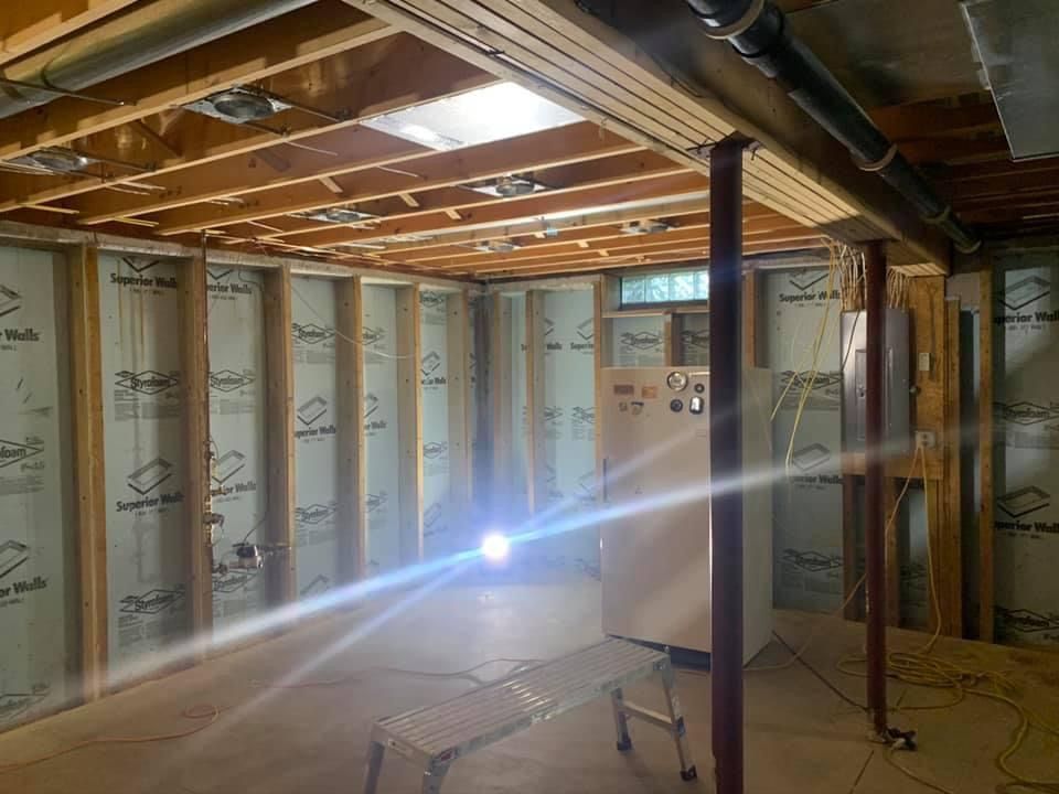 Basement framing with insulation and a light. Red support beams, exposed wooden ceiling, and unfinished walls.