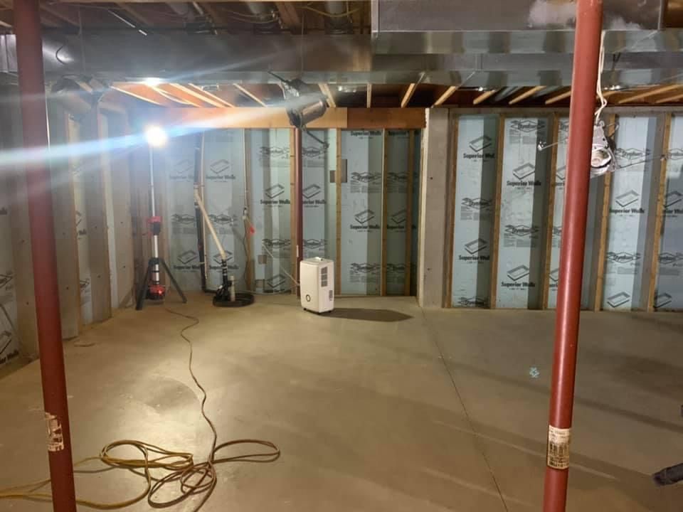 Basement with support beams, insulated walls, and a portable heater. Construction in progress.