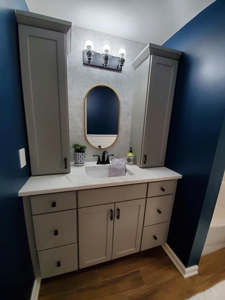 Bathroom with gray vanity, tall cabinets, oval mirror, and blue walls.