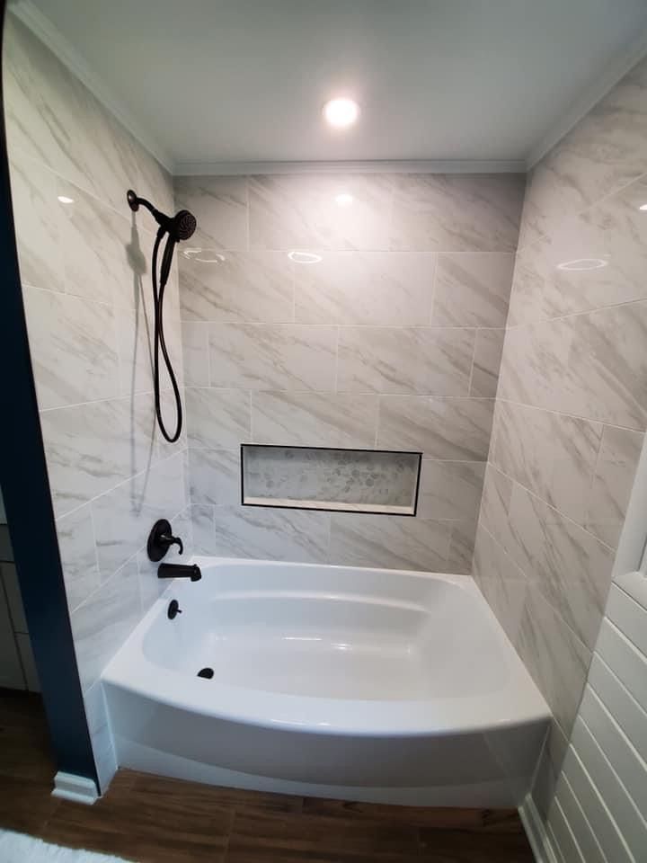 Bathroom with a white tub, gray marble-look tile, and a black showerhead.