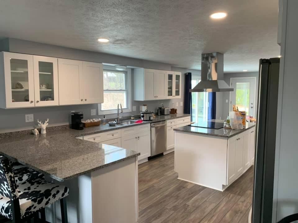 Bright and clean white kitchen with granite countertops, a central island with a custom range hood, featuring Shaker cabinets, stainless steel appliances and new LVP flooring.