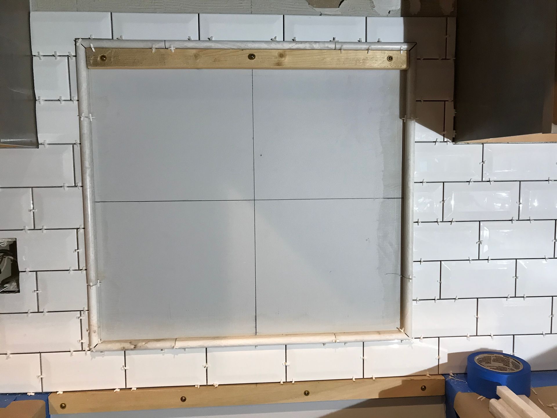 Square window frame surrounded by white tiled wall, with a sheet of frosted plastic inside.