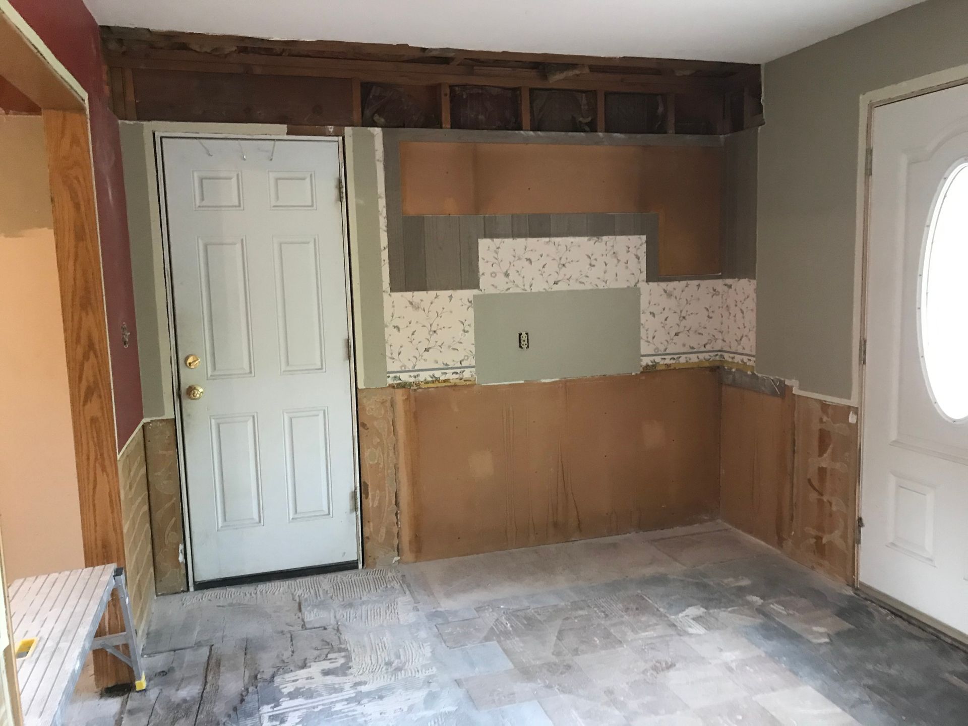 Interior room under renovation with exposed walls, doors, and damaged flooring.