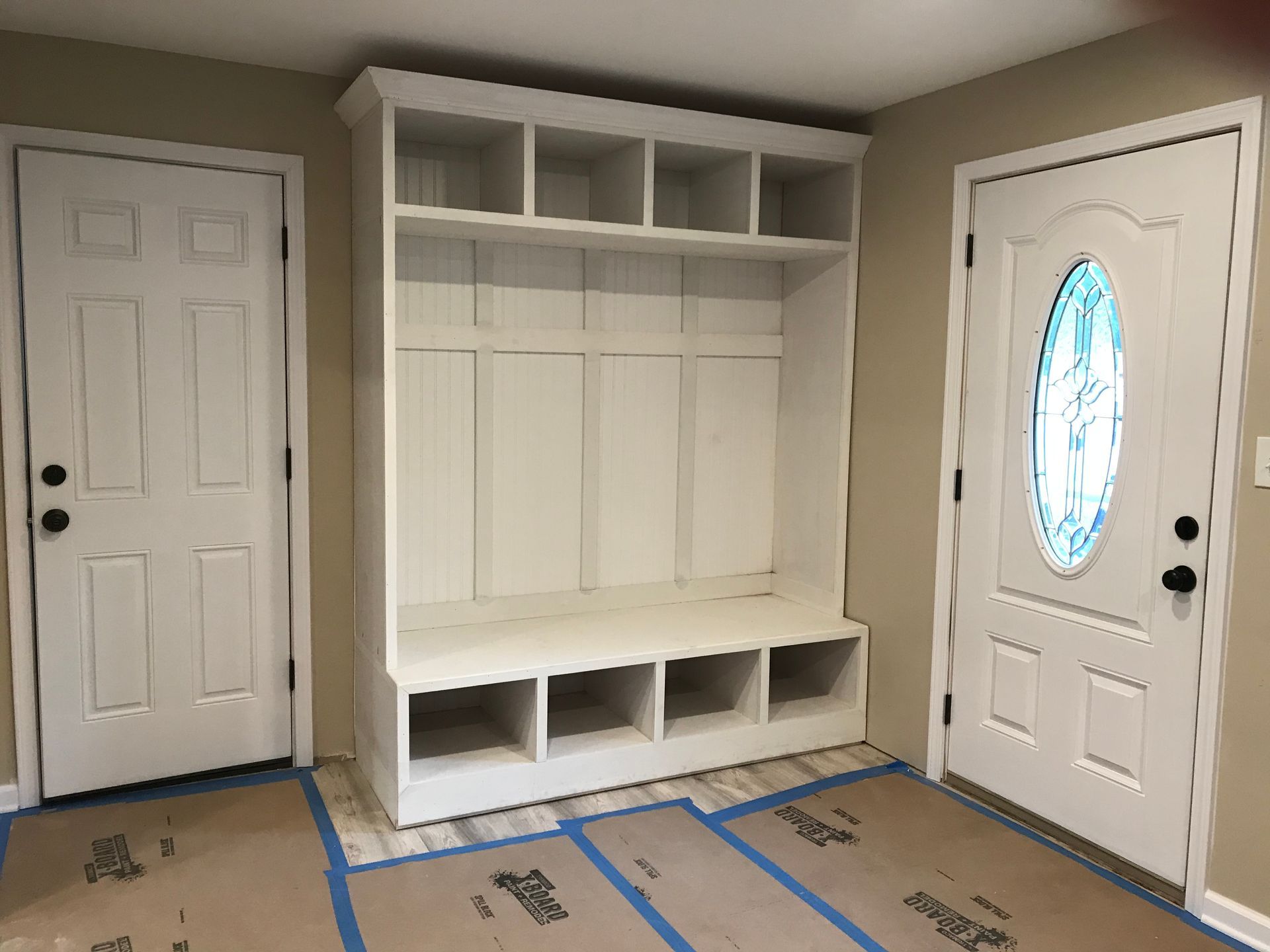 White built-in entryway bench with cubbies and storage. Two doors flank it, one with an oval glass window.