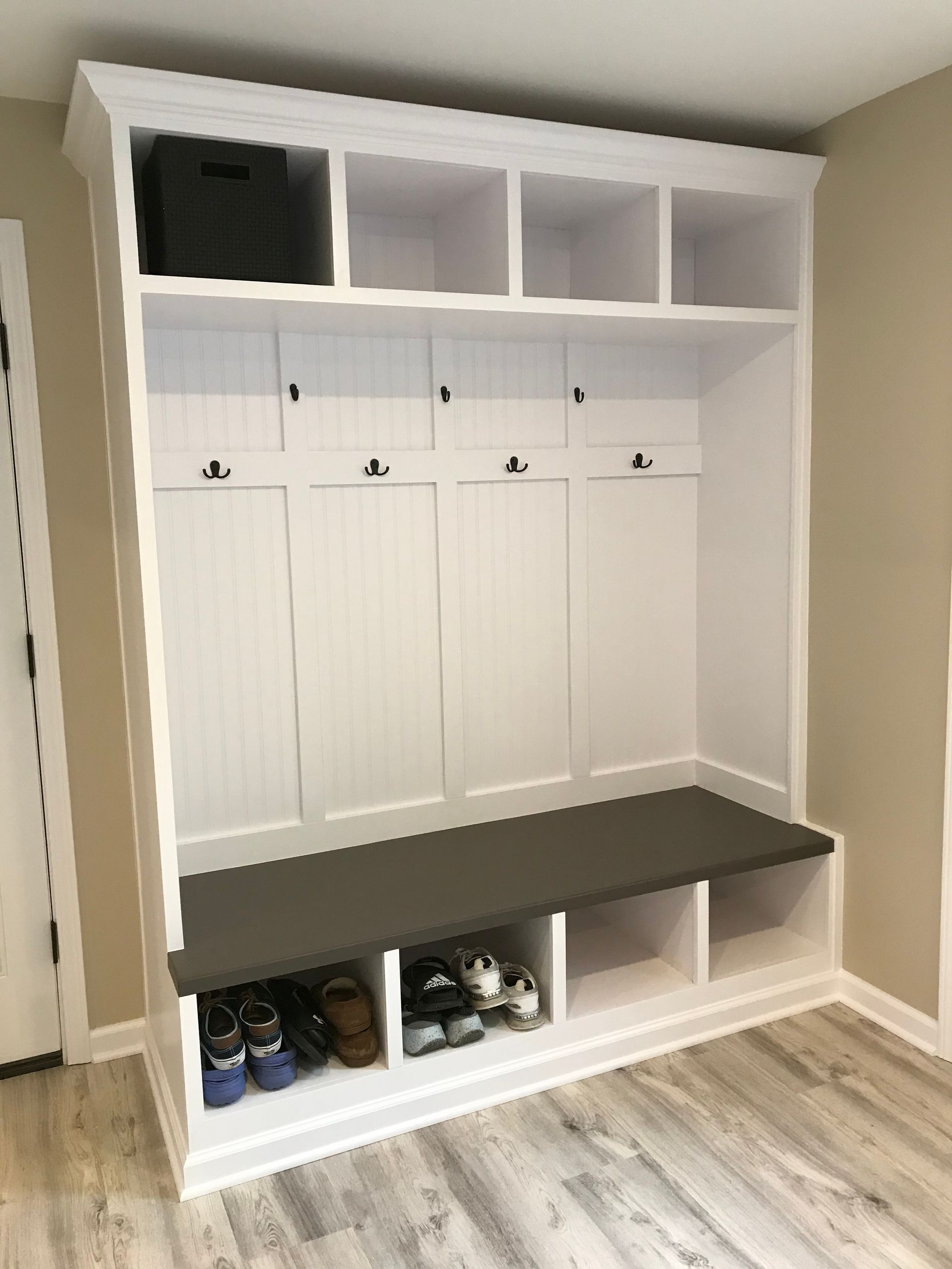 White entryway storage unit with cubbies, hooks, bench, and shoe storage.