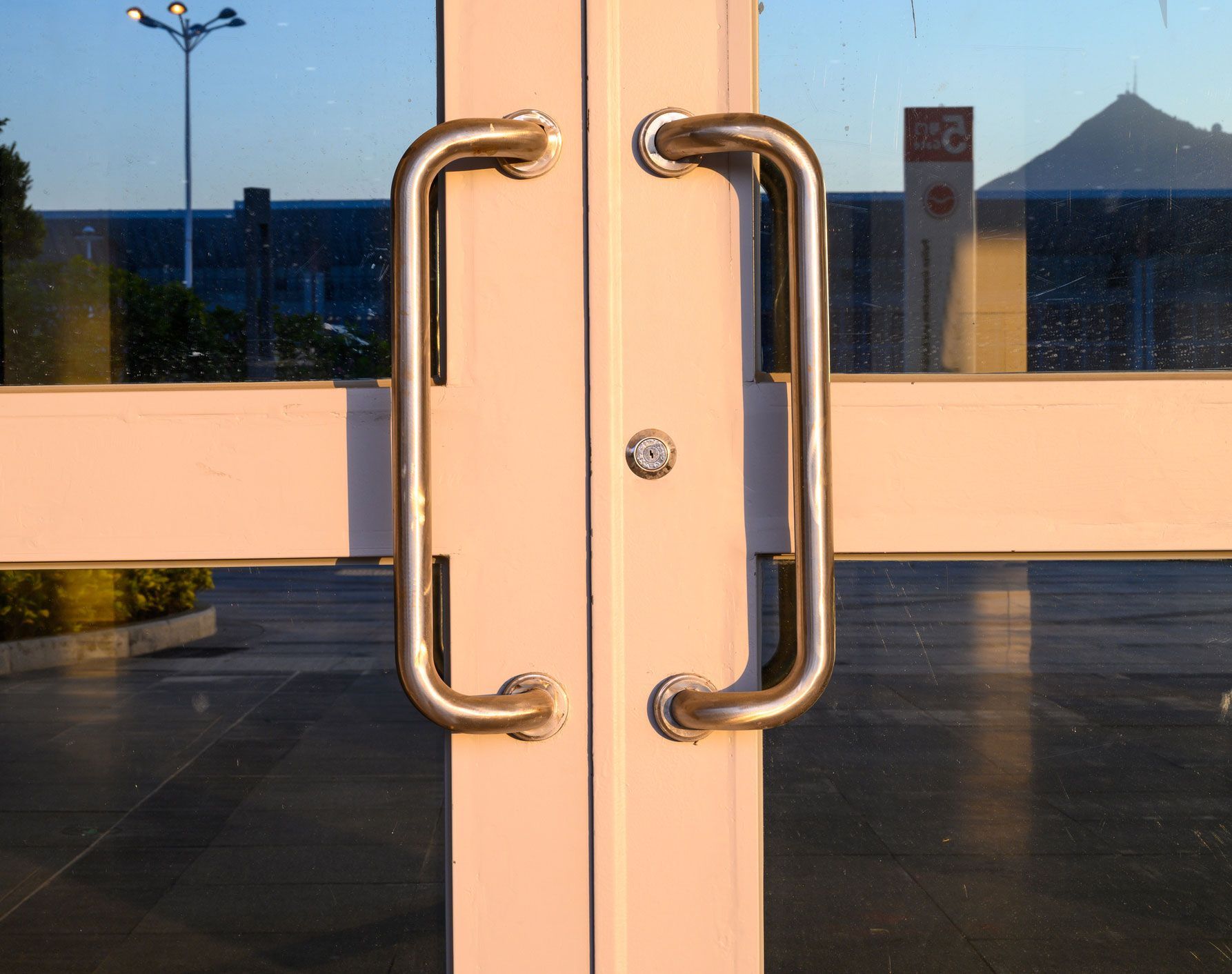 A white door with stainless steel handles is open to a parking lot