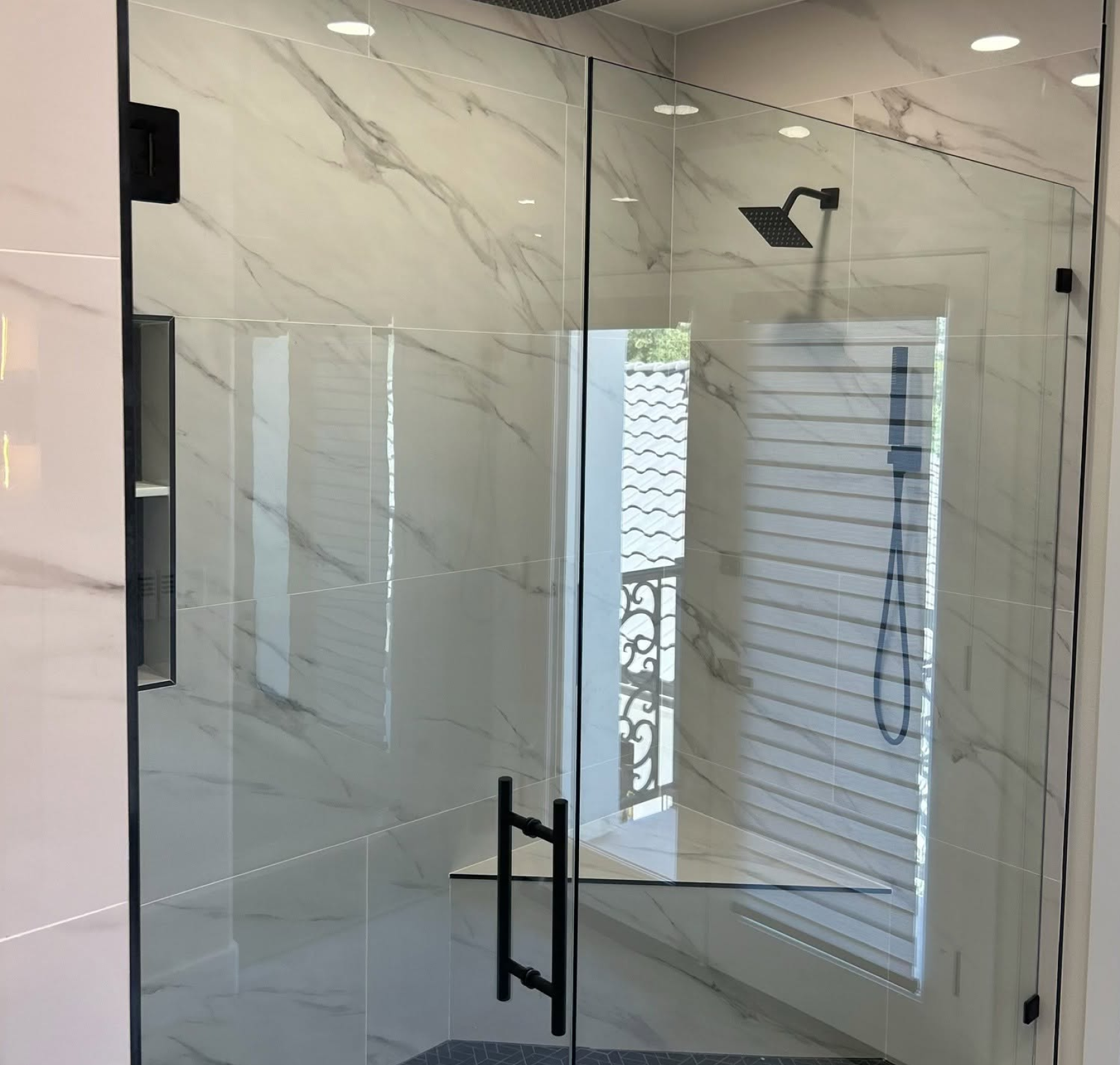 Modern glass shower enclosure with black handles in a bright marble-tiled bathroom