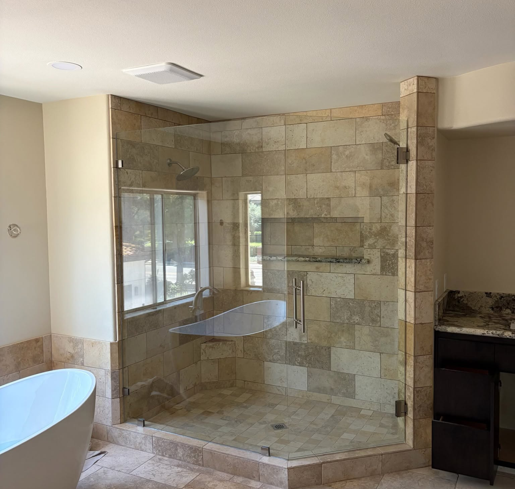 Stone-tiled walk-in shower with glass enclosure in a bright bathroom Stone-tiled walk-in shower with glass enclosure in a bright bathroom