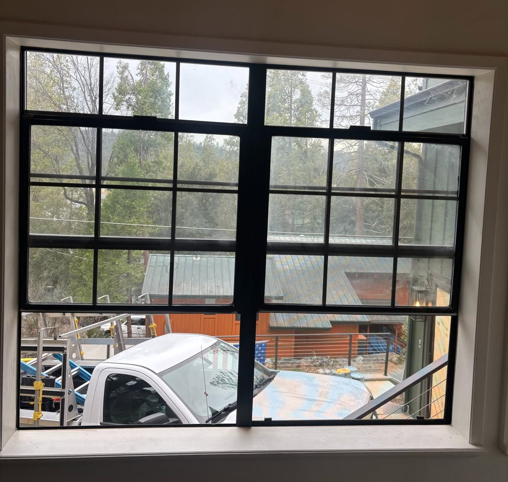 View through a window grid of a rainy yard with cars, a truck, and trees outside