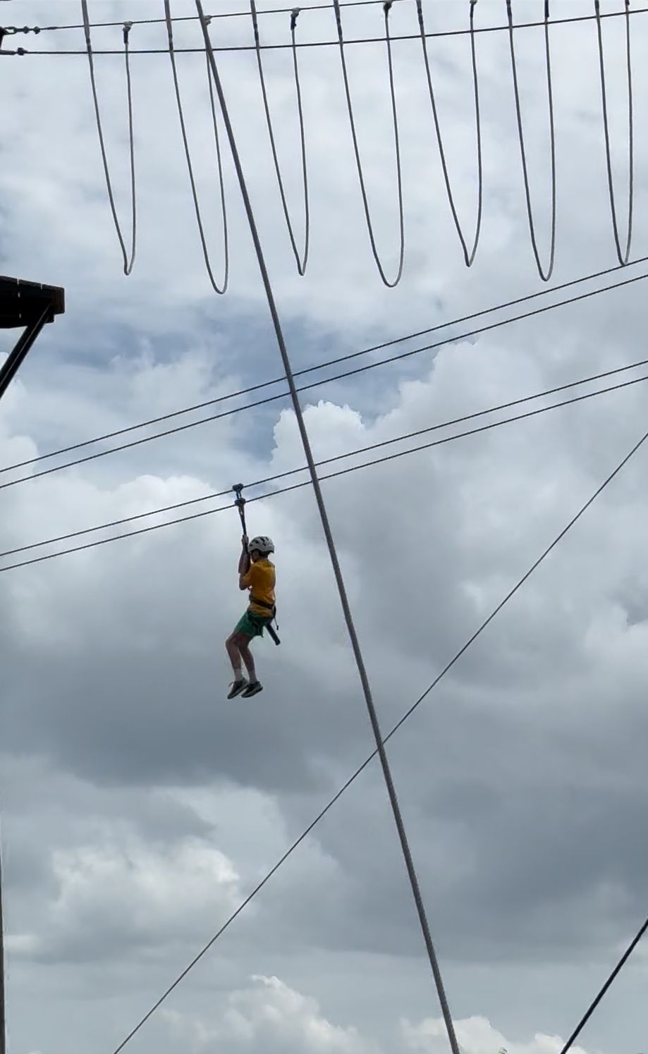 Person ziplining through the air against a cloudy sky, wearing a helmet and harness.