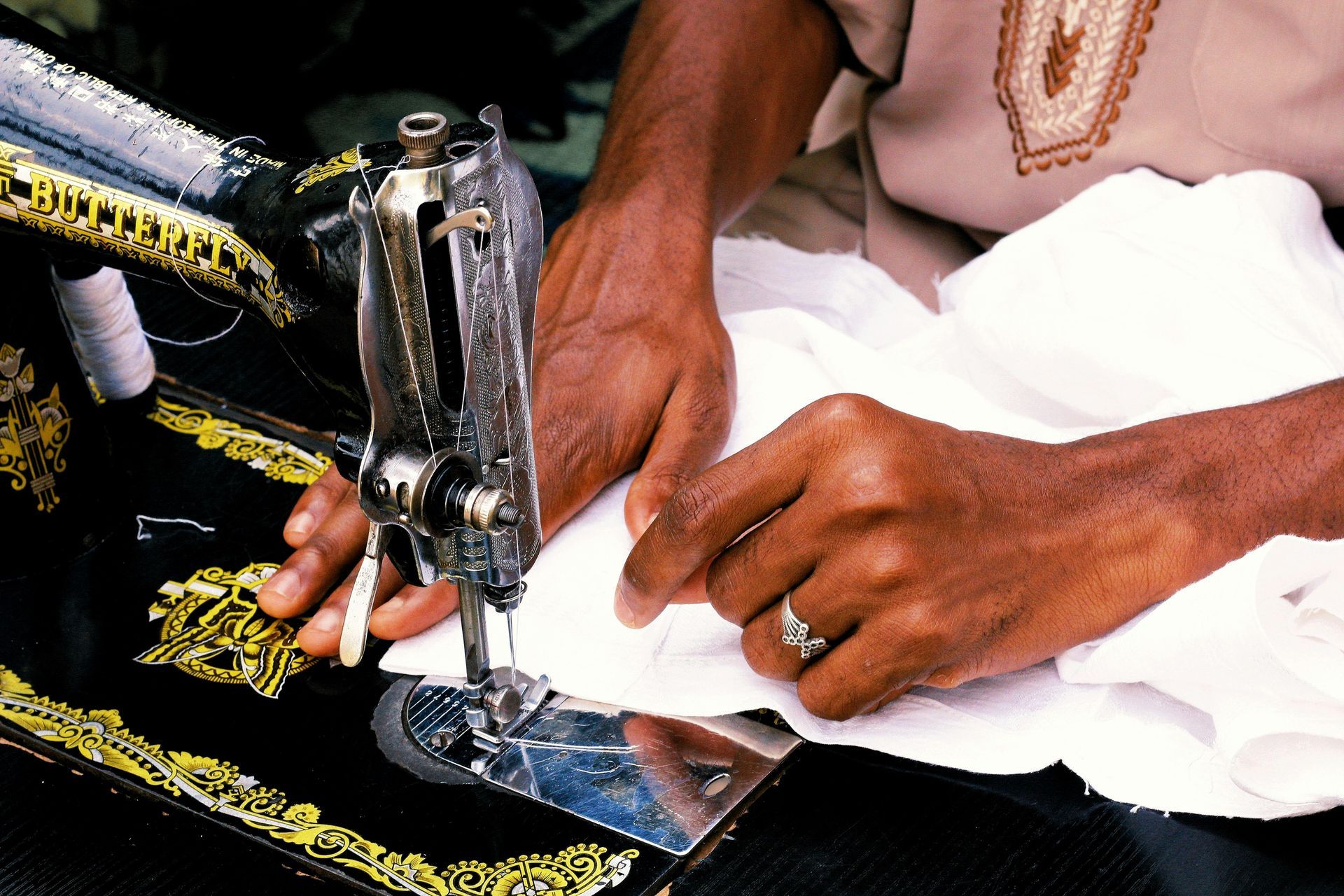 Person sewing white fabric with a vintage black and gold sewing machine.