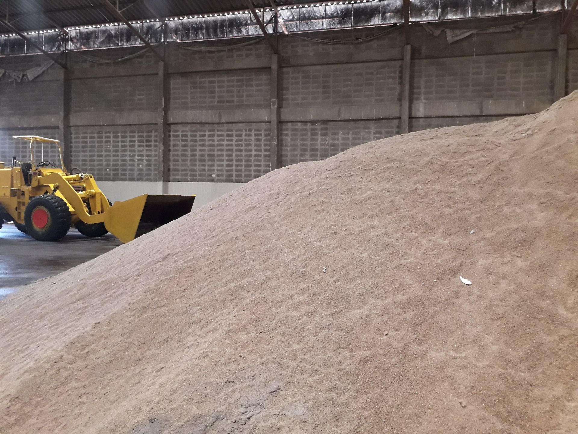 Yellow loader next to a large pile of tan-colored material inside a warehouse.