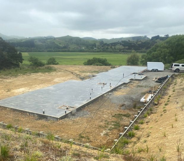 A rectangular concrete foundation for a new building sits on a hillside overlooking a green, rural valley. A rectangular concrete foundation for a new building sits on a hillside overlooking a green, rural valley.
