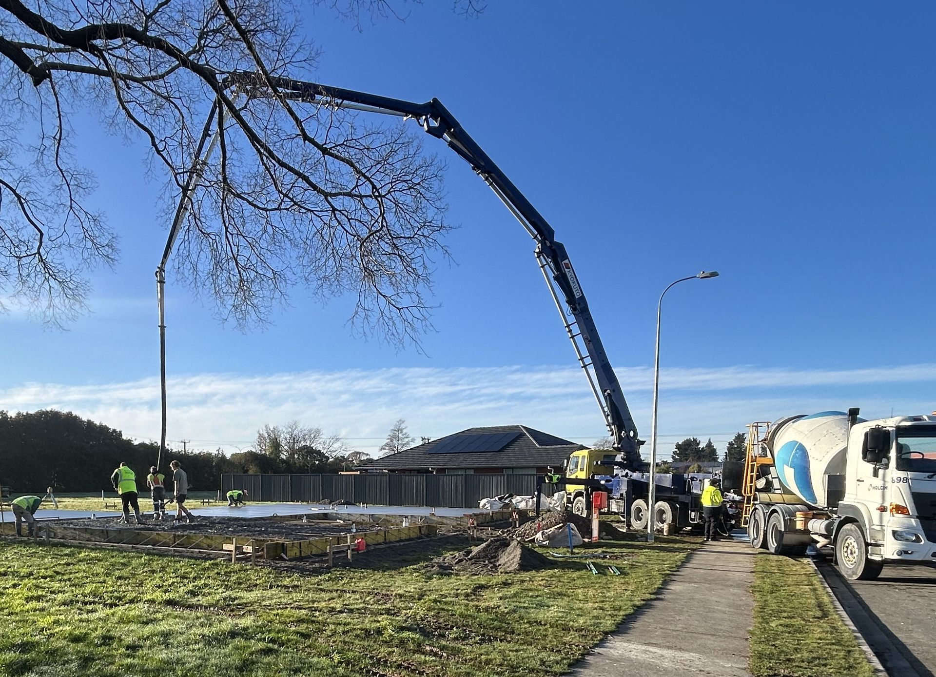Construction workers use a long concrete pump truck to pour wet cement at an outdoor job site on a sunny day. Construction workers use a long concrete pump truck to pour wet cement at an outdoor job site on a sunny day.