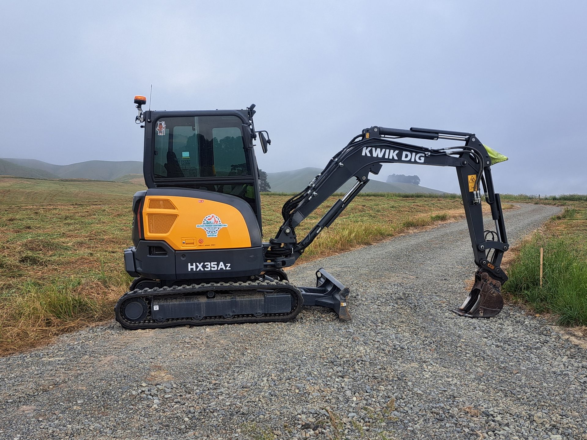 A yellow and black mini excavator parked on a gravel path in a grassy field under a cloudy sky. A yellow and black mini excavator parked on a gravel path in a grassy field under a cloudy sky.