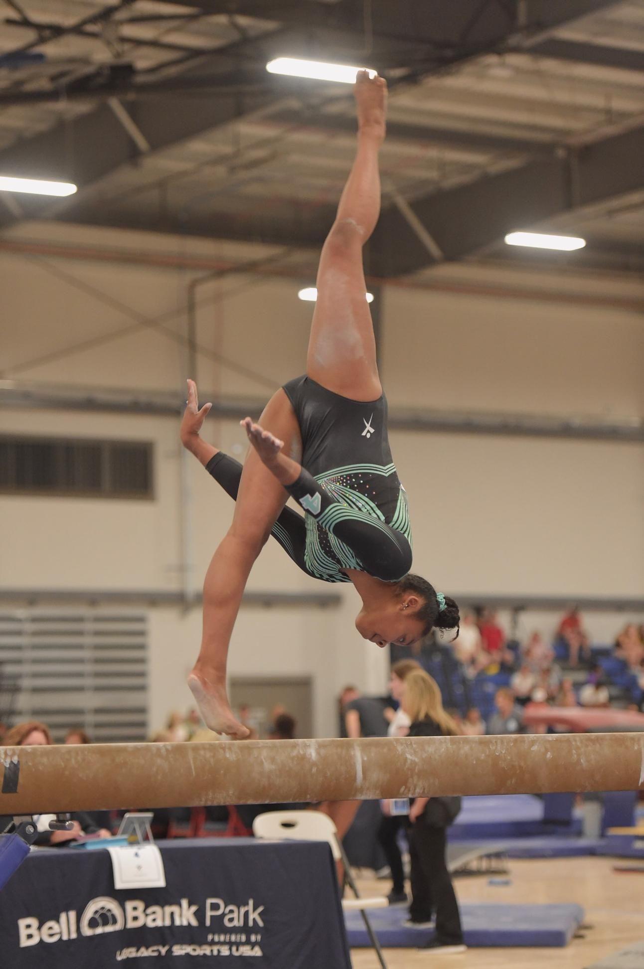 Gymnast balancing on one hand atop a balance beam during a competition indoors