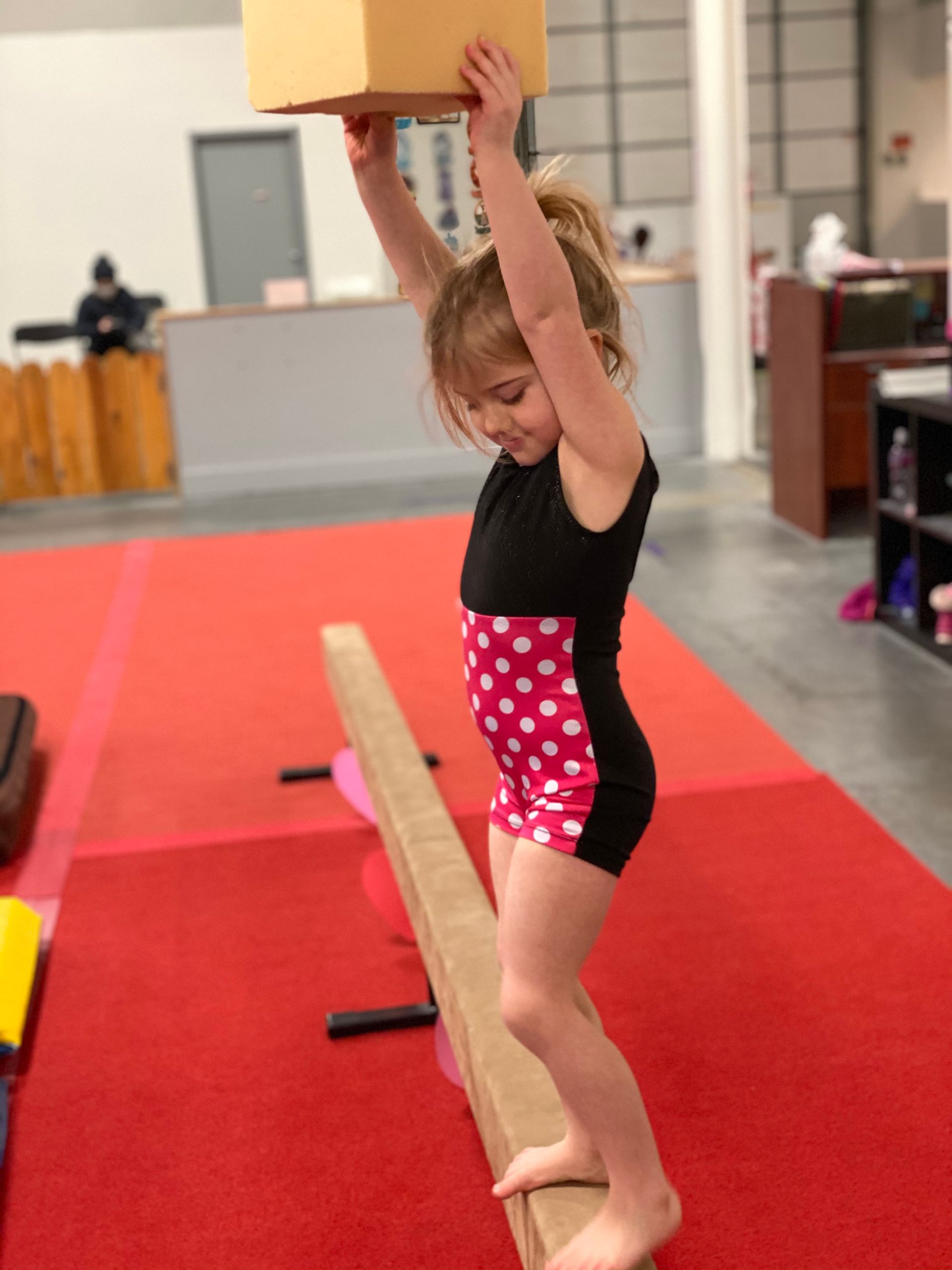 Girl in green shirt doing the splits on a blue mat, smiling.