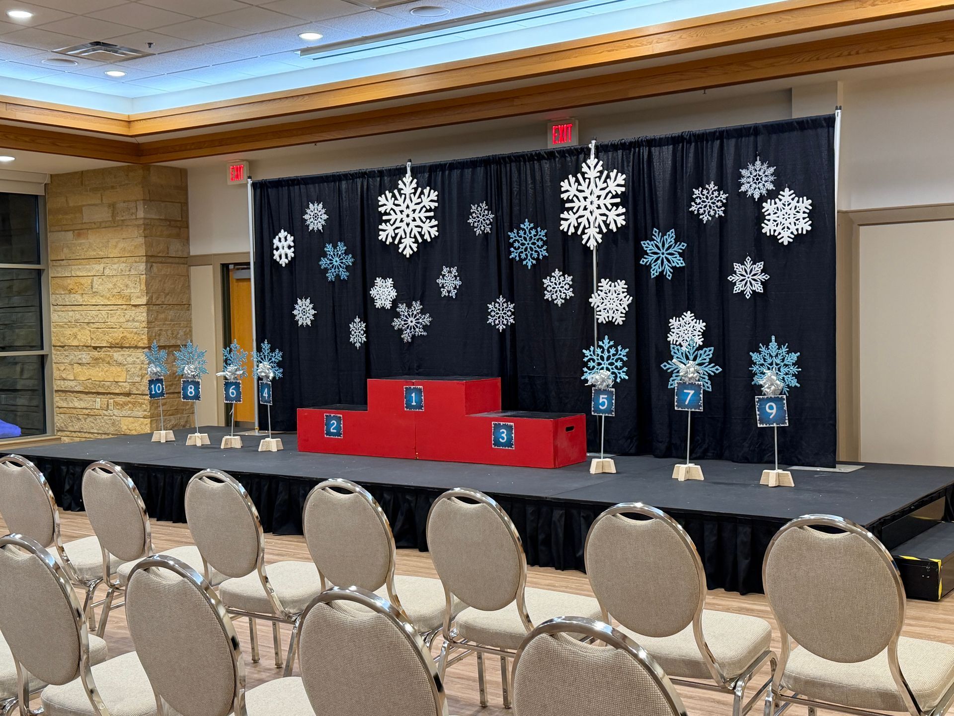 Empty conference room stage with black snowflake backdrop and rows of beige chairs in front