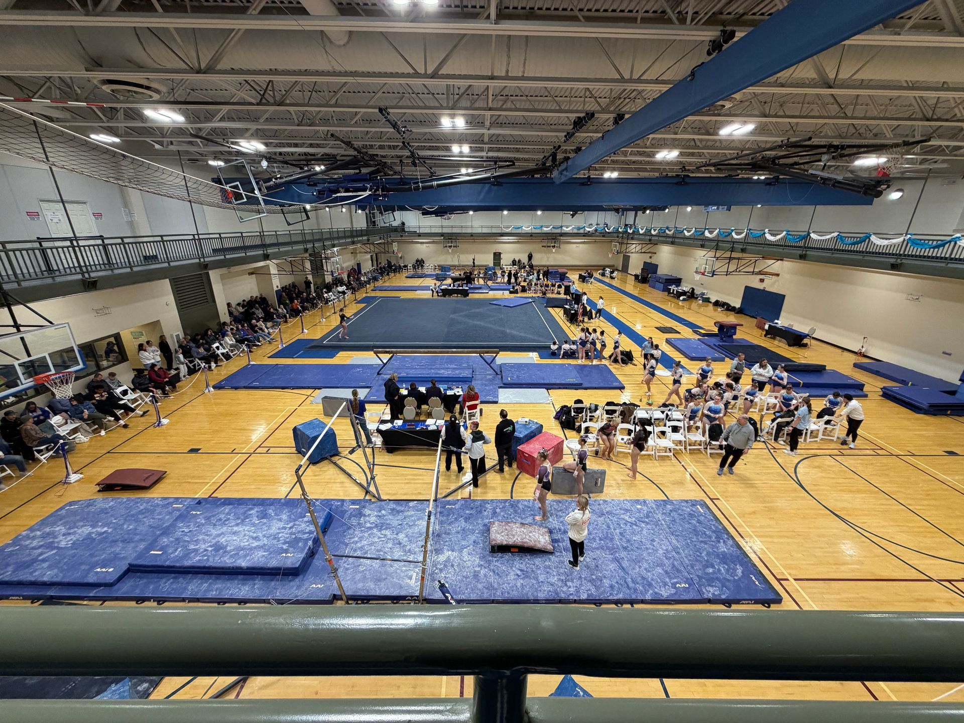 Indoor gymnastics meet with vault, balance beams, and mats in a large gymnasium