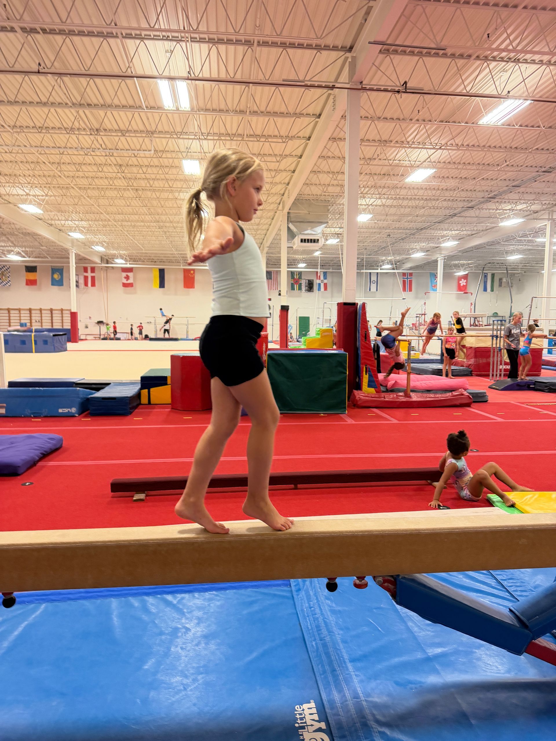 Girl in green shirt doing the splits on a blue mat, smiling.