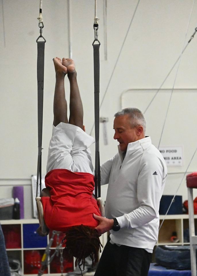Instructor assisting a person hanging upside down on gym straps in a studio