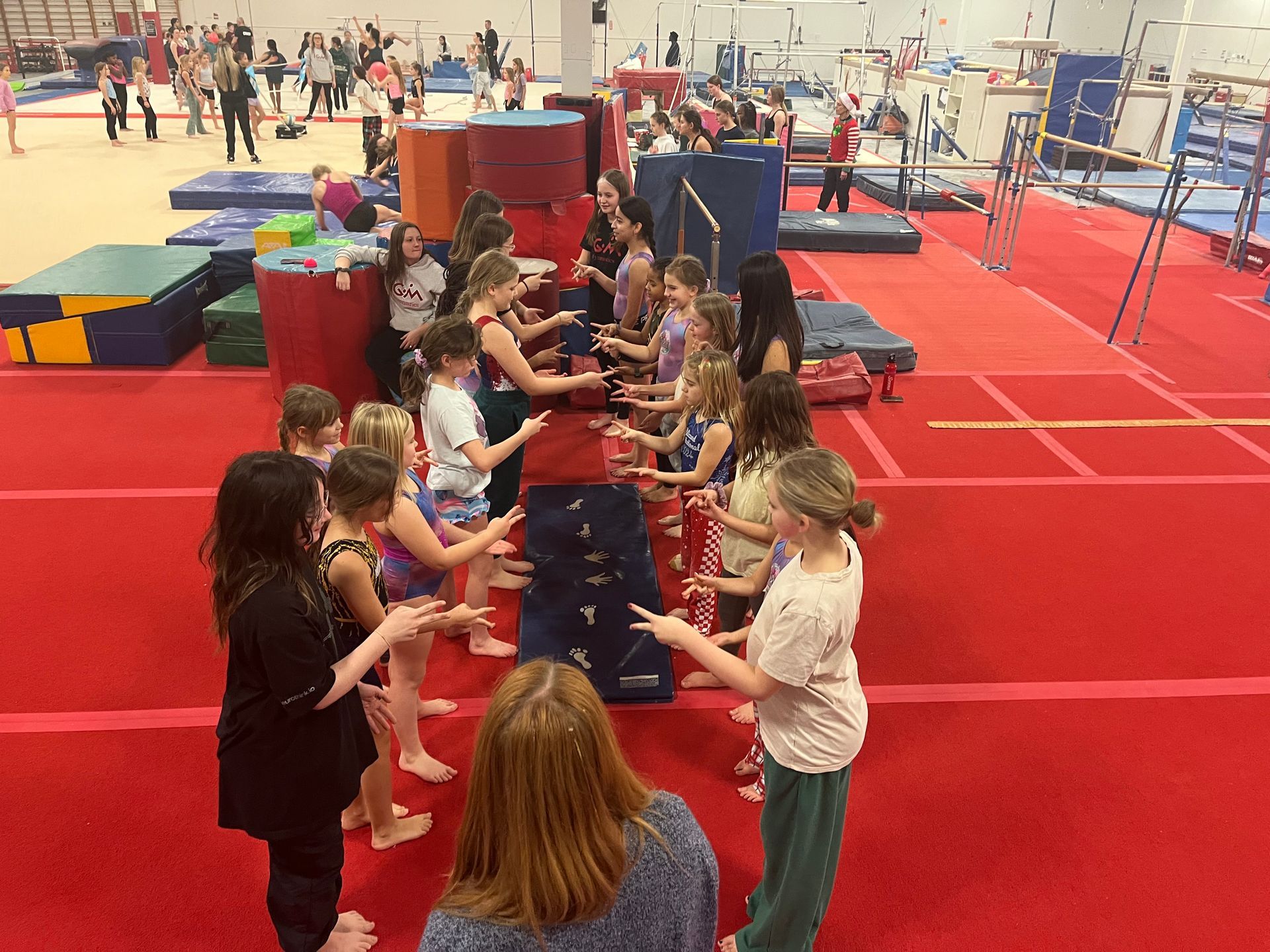 Children on a red mat playing a table game in a busy indoor gymnasium