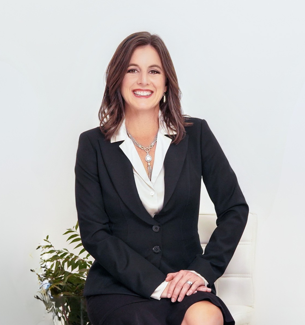 A woman wearing a black jacket and a necklace is smiling.