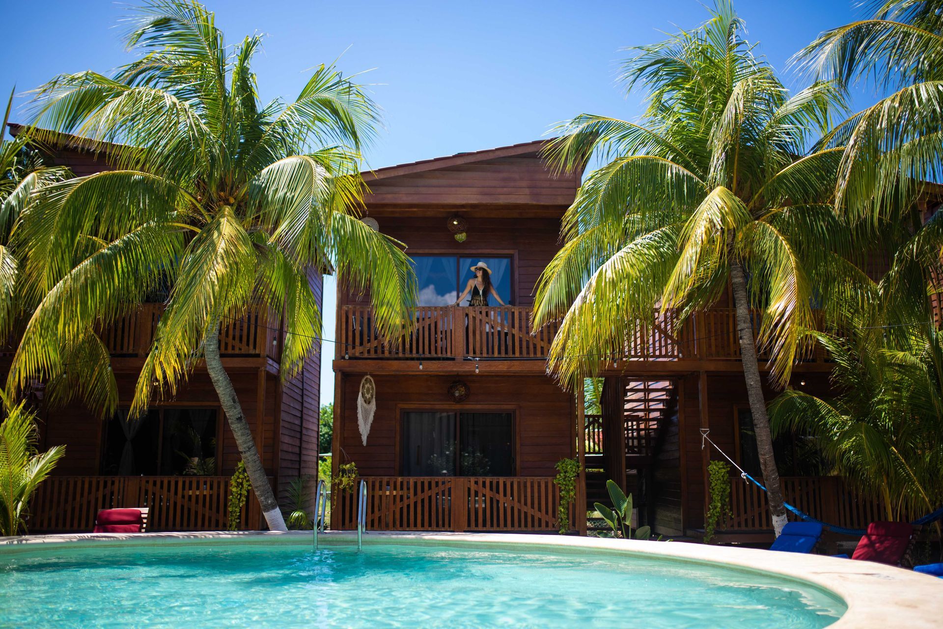 Villa tropical en un complejo turístico con palmeras y una piscina turquesa bajo un cielo azul brillante.