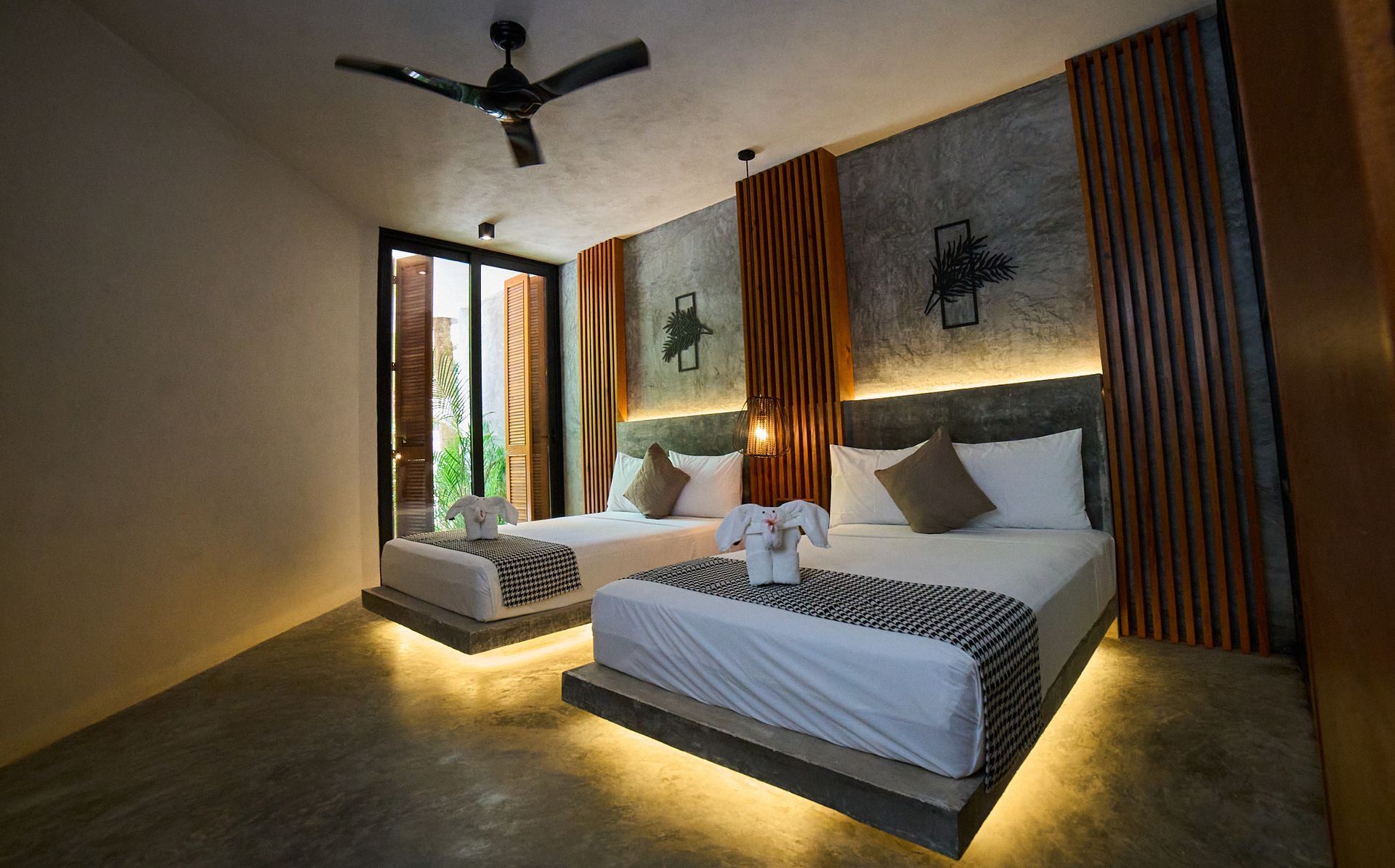 Dormitorio moderno con cama, sofá, iluminación cálida, ventilador de techo y puertas que dan al balcón.