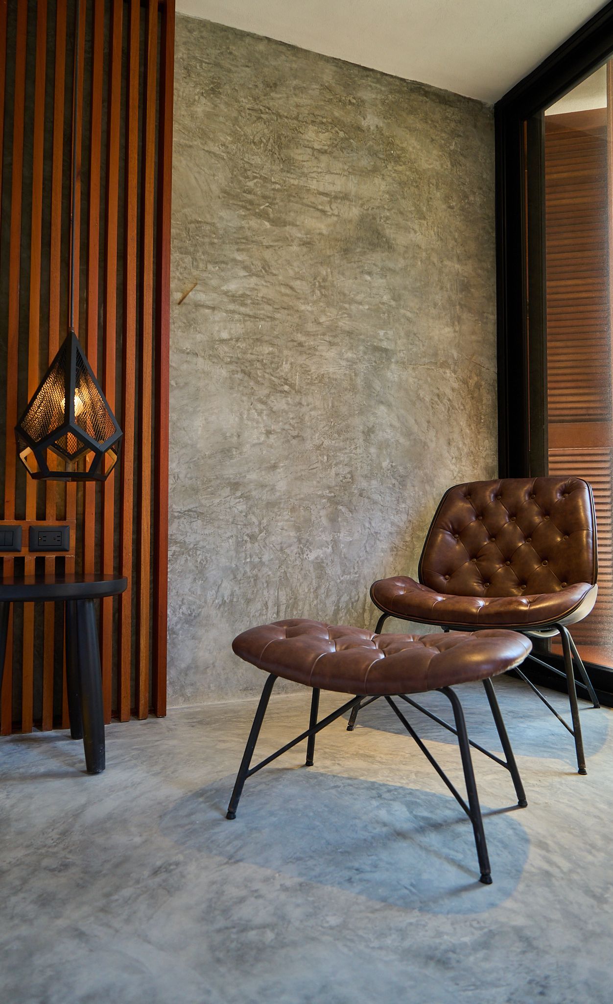Salón moderno con sillón de cuero marrón, lámpara de pie, listones de madera y pared texturizada.