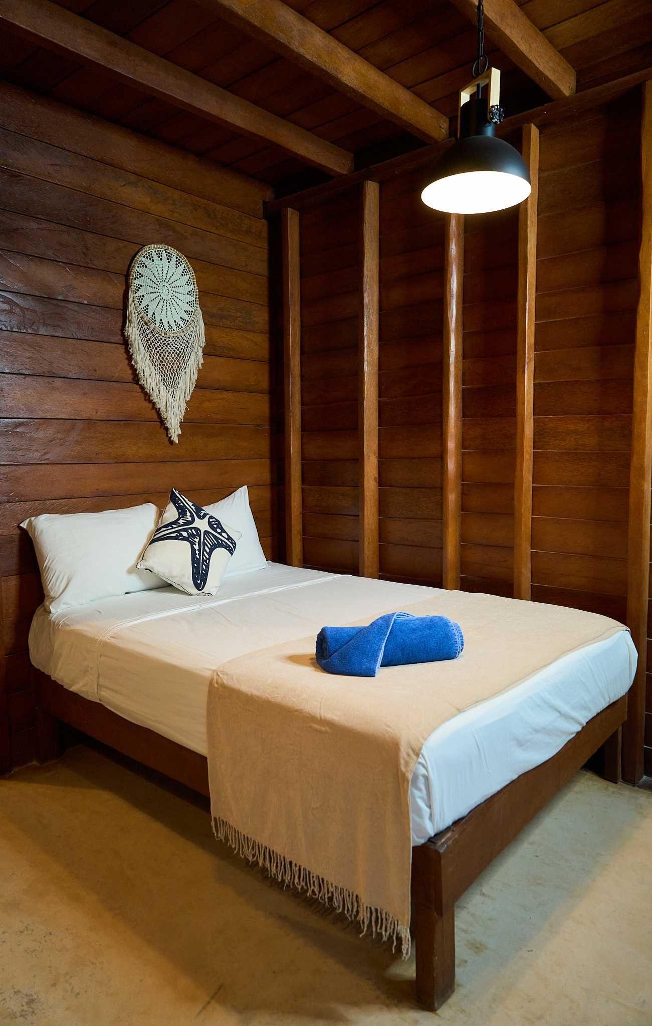Acogedora habitación de madera con una cama bien hecha, toallas azules y una lámpara colgante.