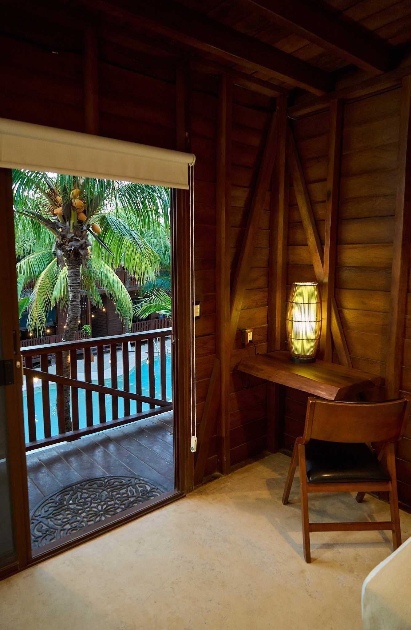 Acogedora habitación con detalles de madera, balcón privado y vistas a la vegetación tropical.