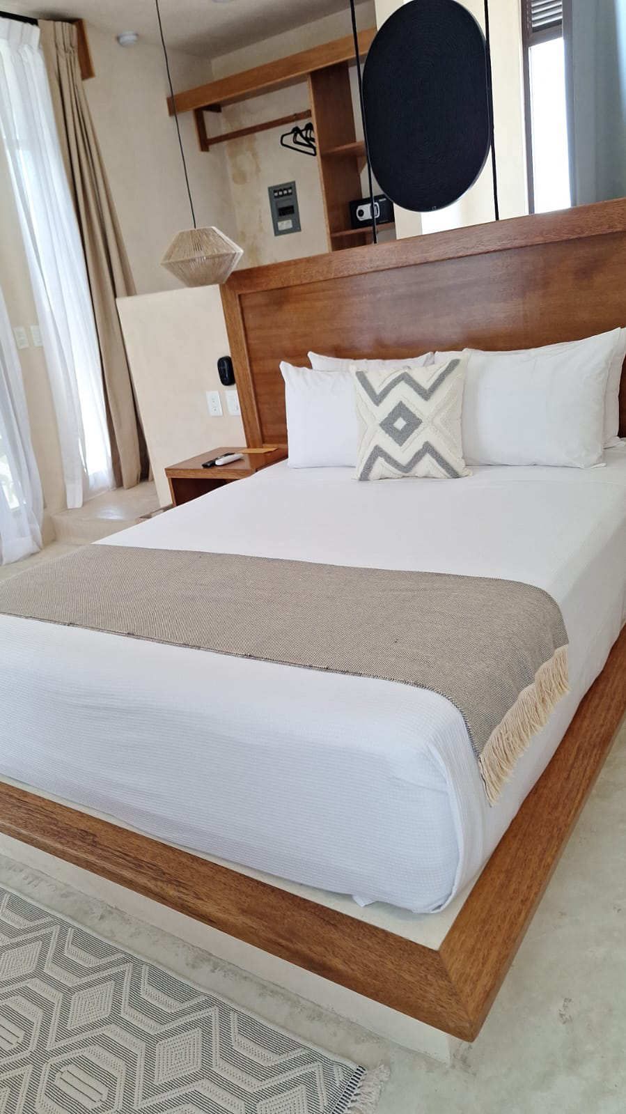 Dormitorio moderno con estructura de cama de madera, ropa de cama blanca, camino de mesa estampado y almohada decorativa.